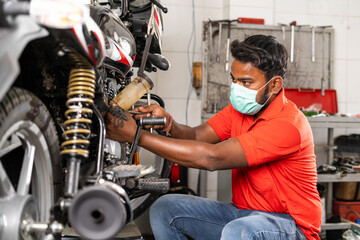 motorbike mechanic busy repairing bike at garage with medical face mask - concept of safety precautions, hygiene and safety measures to protection from coronavirus covid-19 pandemic and pollution