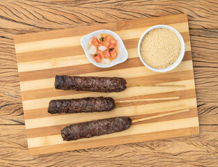 Meat Kafta skewers over wooden board with farofa and vinaigrette