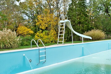 backyard swimming pool with pool slide and ladder emptied out shutting down for winter