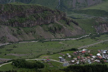 view of the mountain village from a high hill where you can see the green mountains and brown roofs around the village
