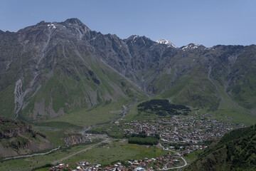 view of the mountain village from a high hill where you can see the green mountains and brown roofs around the village