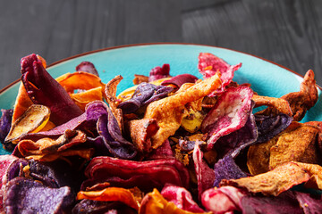 Beet and carrot salty chips in an old blue plate. Dark wood background