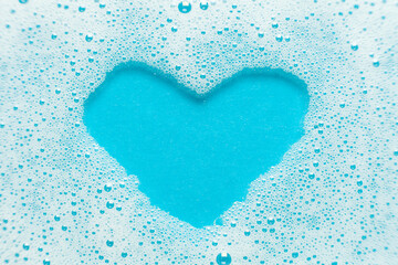 Hygiene and skin care. Soap foam in the shape of a heart on a blue background.
