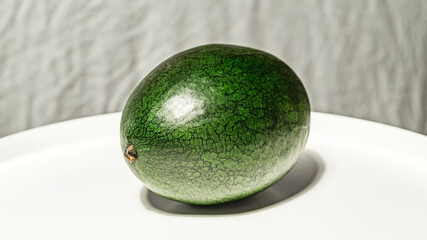 Small, fresh, dark green watermelon of the Dragon's Egg variety on a white-grey background