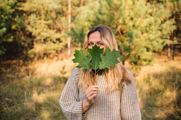 Young attractive walking outdoors and hiding her face behind oak brunch with three leaves
