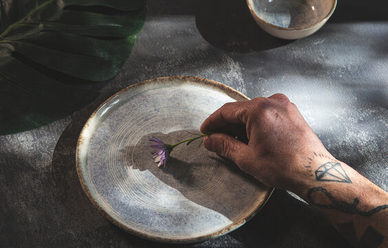 Tattooed man placing flower on ceramic plate