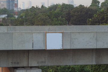 A blank white sign is attached to a concrete bridge.