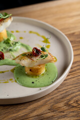 Eating meal in a restaurant with knife and fork, dipping pieces of fish in a green creamy sauce, close up eating