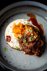 Close up of chopped dark stewed beef with parsnip cream and crispy chips, grey stone dish
