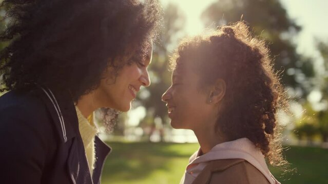 Smiling parent touching noses with cute daughter in golden sunlight portrait.