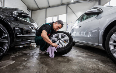 Professional car service worker polishing luxury car rim with microfiber rag or cloth in a car...