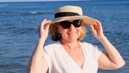 beautiful 50 year old woman in a straw hat and sunglasses on a blue sea background. Summer,...