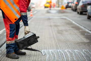 A worker pours liquid asphalt, molten bitumen from a bucket of resin.