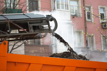 Road milling machine removes old asphalt and loads milled asphalt into the dump truck.