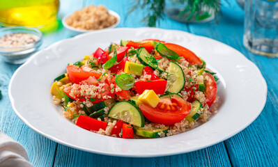 Fresh salad with vegetables, quinoa and fresh herbs on a blue background.