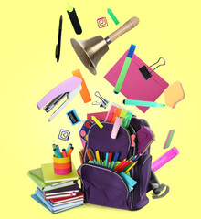 Backpack, school bell and different stationery flying on yellow background