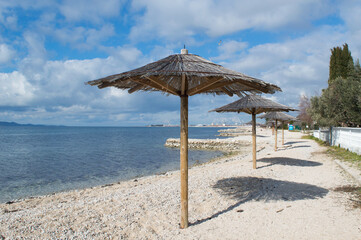 Pebble beach with straw parasol in small town Bibinje close to Zadar in Croatia, concept of relaxing vacation - obrazy, fototapety, plakaty