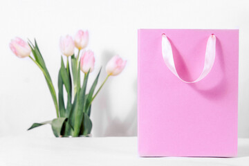 A pink gift bag with delicate tulip flowers on a white background. Discounts and sales for the spring women's holiday on the eighth of March