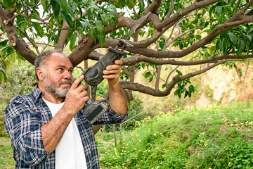 Seasonal pruning of trees. Mature bearded gardener pruning  trees with reciprocating saw in the orchard. Taking care of garden. Cutting tree branch. Spring gardening.
