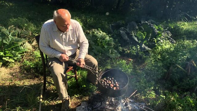 Elderly man roasting chestnuts on the fire.