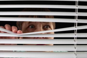 Fototapeta An elderly woman peers through the blinds through the window. obraz