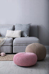 Stylish knitted poufs near sofa in living room. Interior element