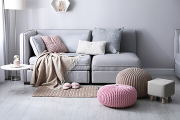 Stylish poufs and ottoman near sofa in living room. Interior element