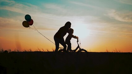 Happy family. Mom teaches her son to ride bike. Family bike ride on green grass. Mom helps her son on bicycle. Happy family on green grass. Mom helps her son on a bike ride. Happy family concept