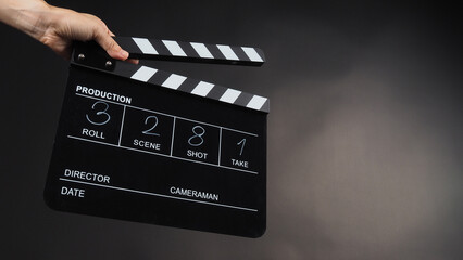 Fototapeta na wymiar A hand is holding a black clapper board or movie slate on black background. It has been written in numbers.