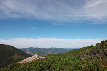 Man with backpack on rocky peak in mountains, back view