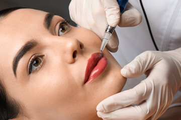 Young woman undergoing procedure of permanent lip makeup in salon, closeup