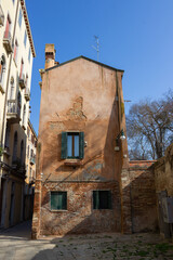 Fototapeta na wymiar Glimpse of Venice. Detail of a small red brick building and peeling plaster. Vertical image.