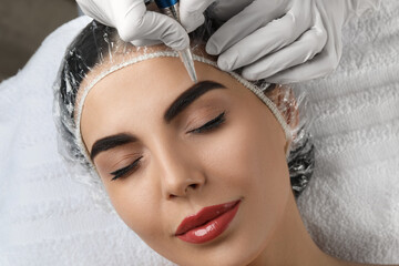 Young woman undergoing procedure of permanent eyebrow makeup in salon, closeup