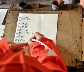 Unrecognizable person writing  medieval font alphabet with a quill pen and inkwell on ancient desk