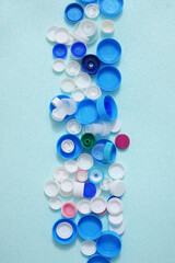 Stripe of colorated plastic bottle caps on a light blue background. View from above.
