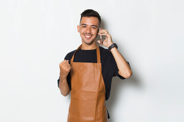 Happy joyful young man barista bartender or waitress using mobile smartphone on white background
