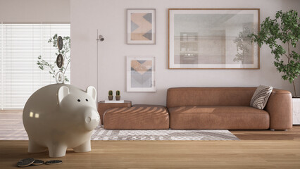 Wooden table top or shelf with white piggy bank with coins, modern bright living room with sofa, expensive home interior design, renovation restructuring concept architecture