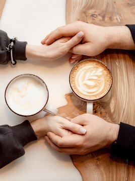 Loving couple holding hands with coffee on a white wooden table. Photo taken from above, top view with copy space, free space, two cups of coffee, man and woman