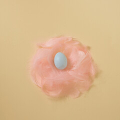 Creative pastel Easter composition with minimal yellow background, pink feather nest and light blue egg