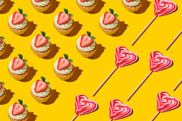 Pattern made of home cookies with strawberries and heart-shaped lollipop on a yellow background. cupcake with big strawberry on top.  Red and whie striped sweet lollipops. Flat lay style.