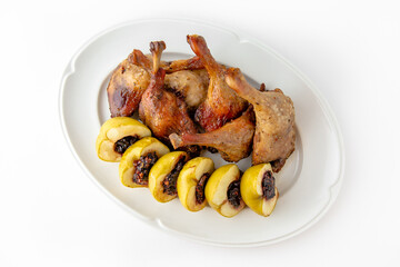 Duck leg confit with baked apples stuffed with dried fruits and nuts on a white plate. Banquet festive dishes. Gourmet restaurant menu. White background.