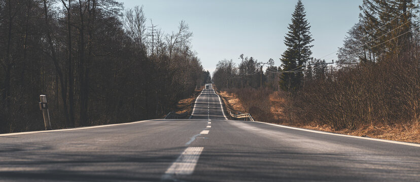 straight, long road with a truck that is visible far in the background. There are trees and various grates around the road. The weather is sunny and the sky is cloudless.