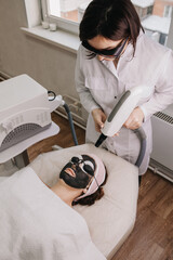 On girl's face, gel with carbon was applied and black goggles were worn. beautician in protective...