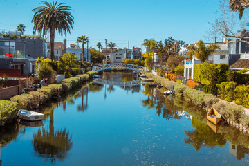 Fototapeta premium Legendary Venice beach water canal in California with blue water and sky, boats, a cute bridge and palm tree.
