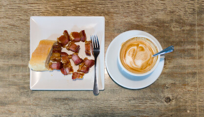 cup of coffee latte accompanied by torrezno skewer, piece of bread and fork and teaspoon