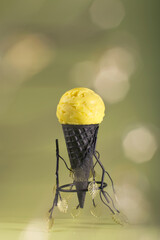 Homemade yellow fruit flavored ice cream in a dark waffle cone on a light background. Healthy...