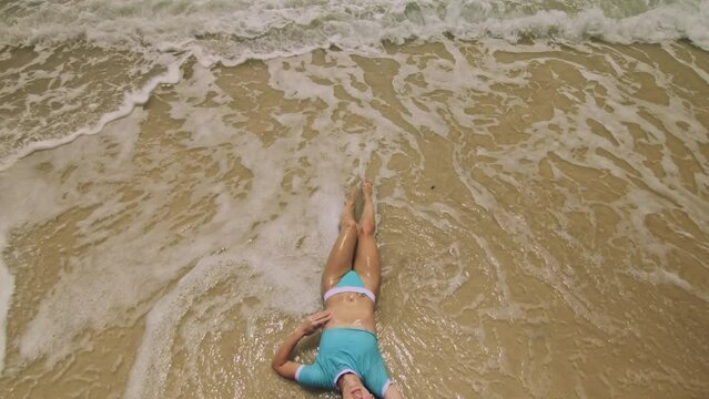 Crazy madwoman daring funny woman lying on shallow water sea. Top view happy slightly tipsy woman enjoying her vacation on a tropical island. Smiling girl funny posing. Concept summer holidays