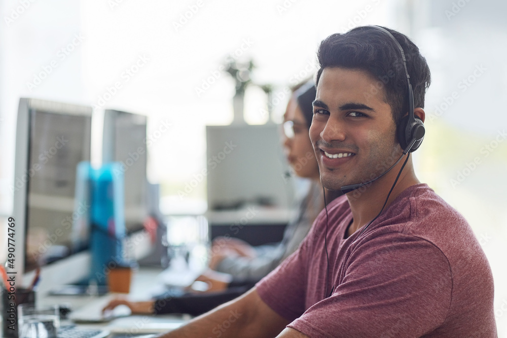 Poster Hes next in line for a promotion. Shot of a young man wearing a headset with his colleagues blurred in the background.