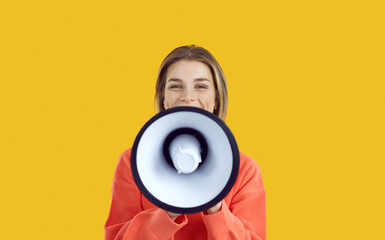 Studio shot of happy beautiful young woman speaking or shouting in megaphone. Pretty college or university student girl with loudspeaker making important announcement isolated on colour background