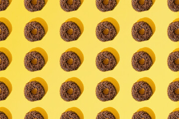 Arranged ring donuts with chocolate glaze. Small brown crumbs on a yellow pastel background. Pattern. Flat lay.